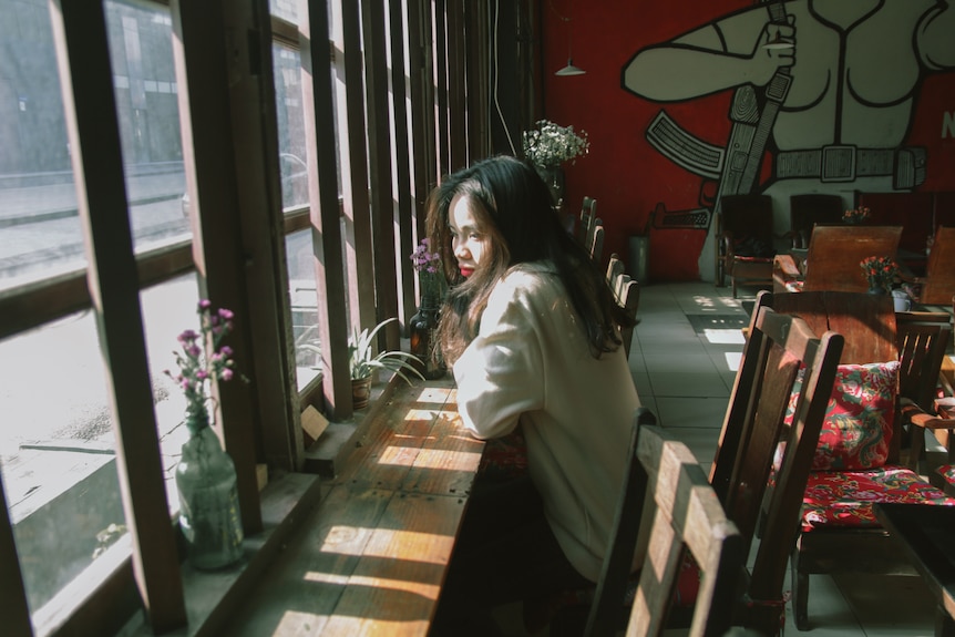 A woman sits alone in a cafe, looking out the window