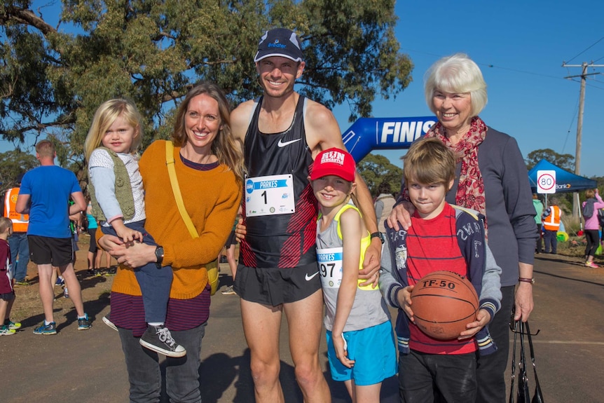 A family standing in front of a blow up finish line including a man in running gear with a number 1 entry plate on his chest