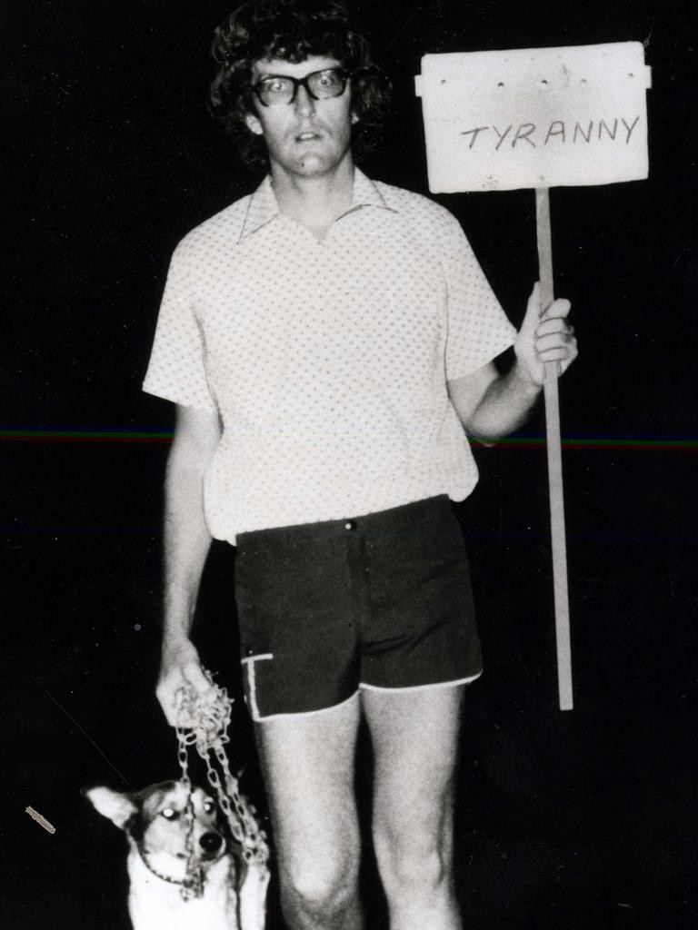 An old photo of a man with glasses holding a sign and accompanied by a dog.