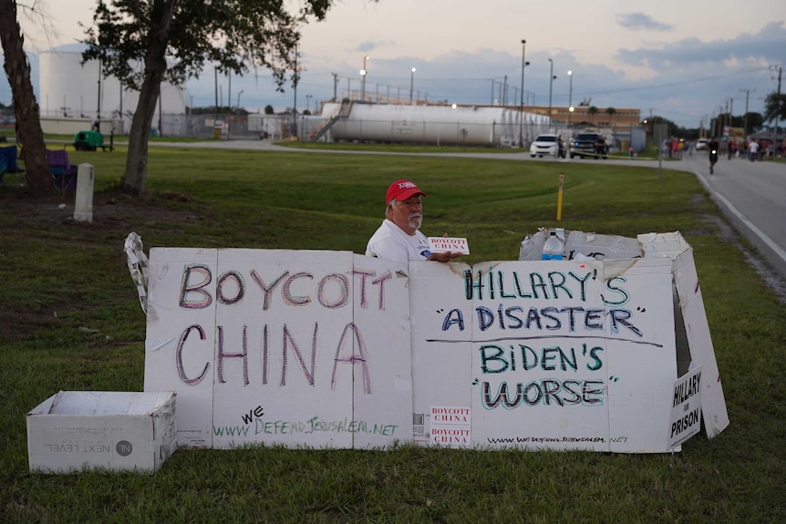 A man sits in a field with signs reading 'boycott China'