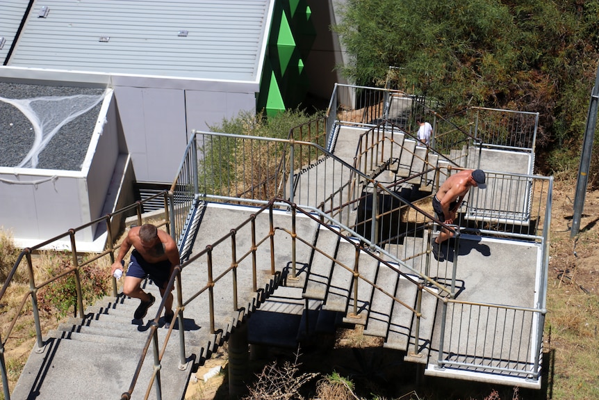 Two men climb up a flight of outdoor stairs