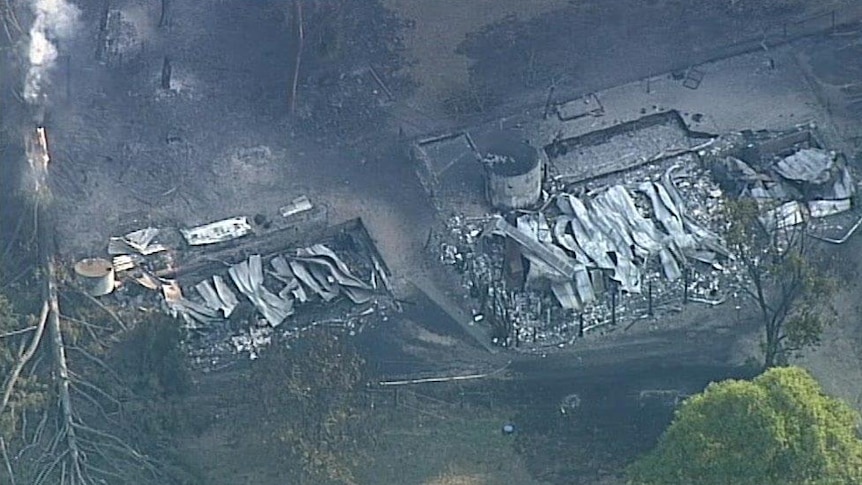 Blackened ground and burnt trees surround the burn-out remains of a house.