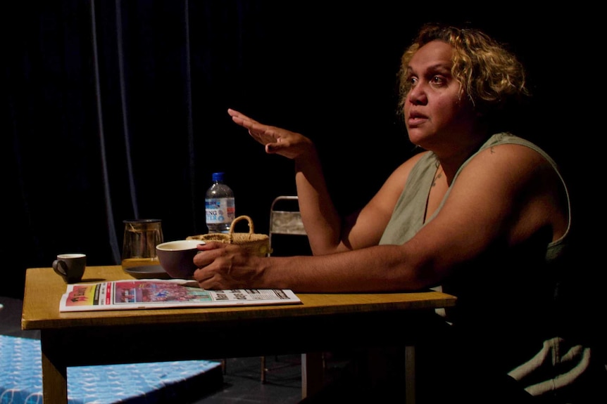 Indigenous woman sitting at desk with coffee cup making a point with her hand talking to left of photo