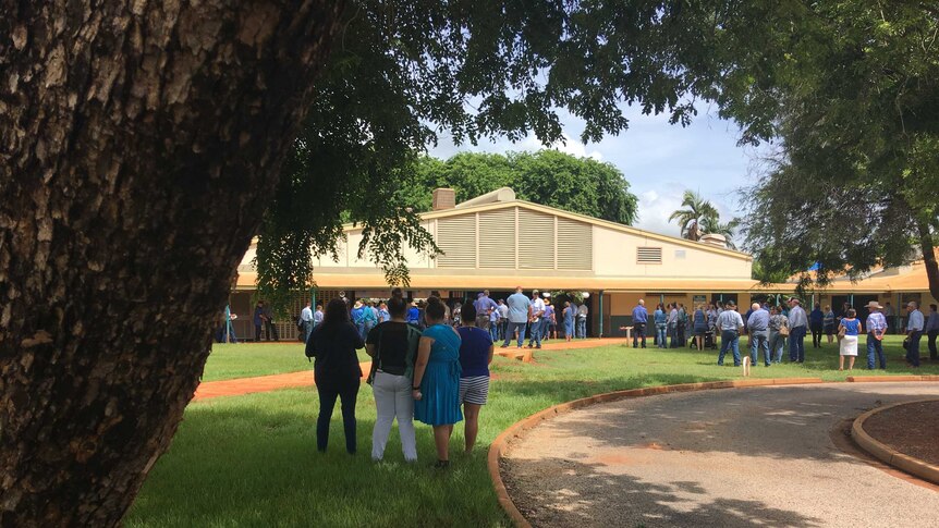 Hundreds of mourners wearing blue gather outside a school building.