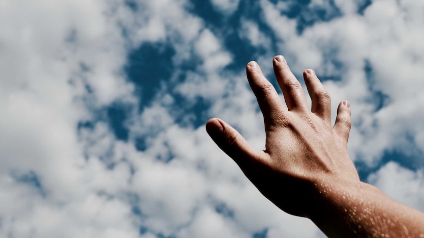 A hand reaches out to a blue sky with clouds
