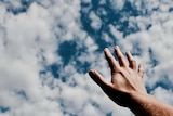 A hand reaches out to a blue sky with clouds