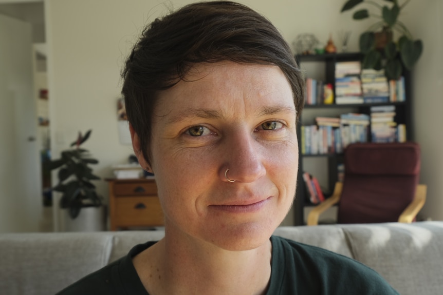 A close up portrait of a woman with short brown hair and a nose peircing.