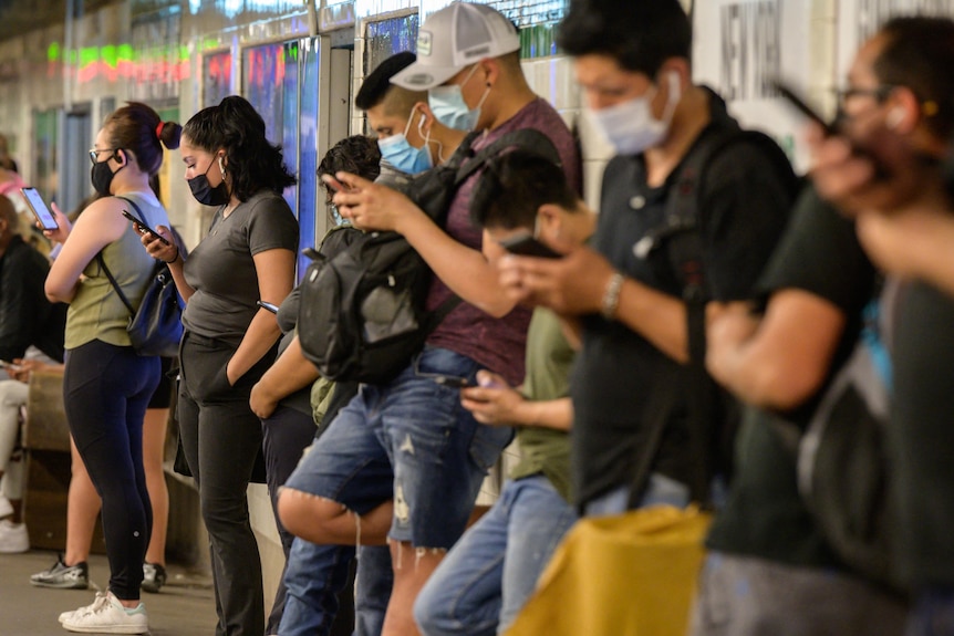 A crowd of people waiting for a train check their phones.