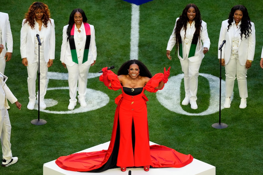 Sheryl Lee Ralph on stage in a red dress with arms raised surrounded by people in white.