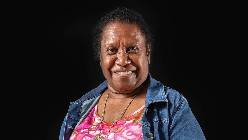 Gail Mabo stands wearing denim jacket and colourful dress