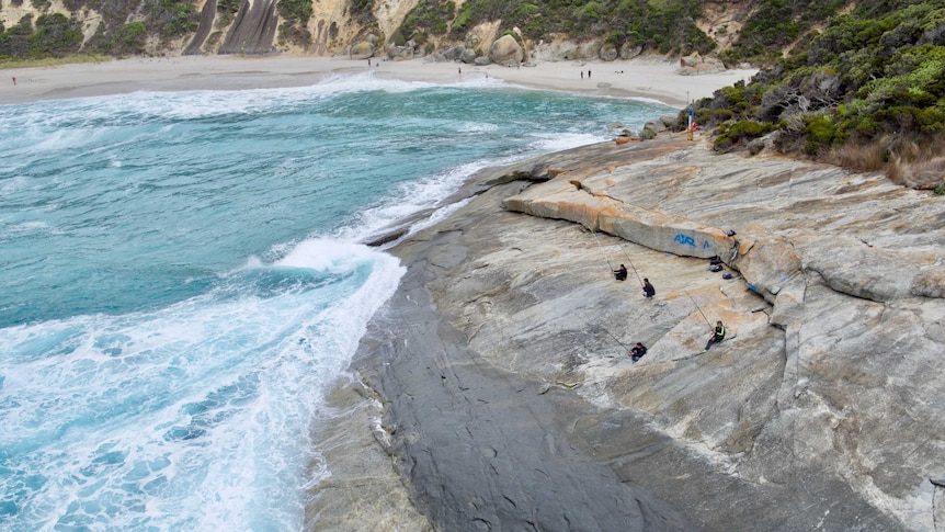 An aerial view of fishermen on rocks with a beach in the background.