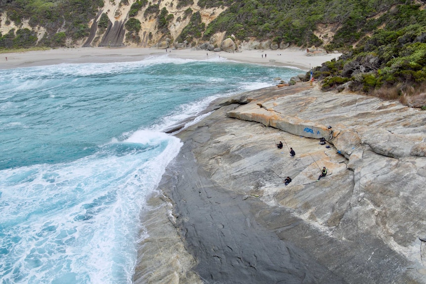 An aerial view of fishermen on rocks with a beach in the background.