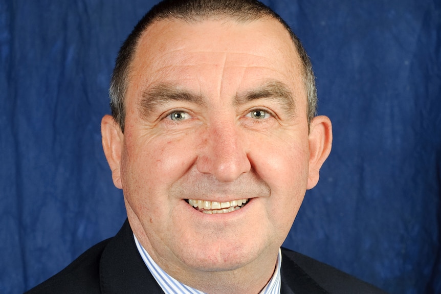 A headshot of a smiling man of late middle-age, wearing a suit.