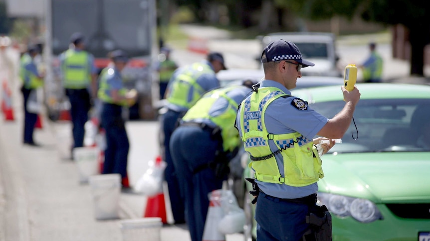 Police officers holding testing machines with a row of cars.