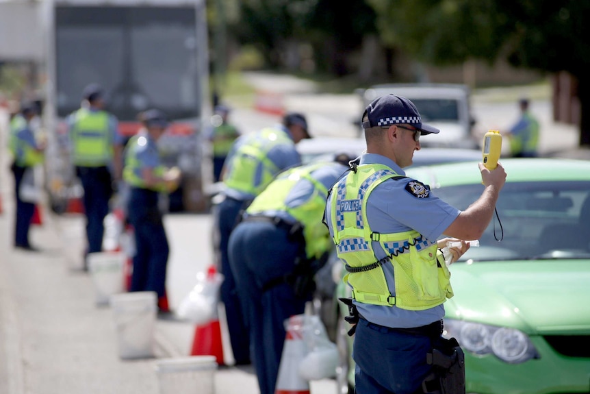 Police officers holding testing machines with a row of cars.