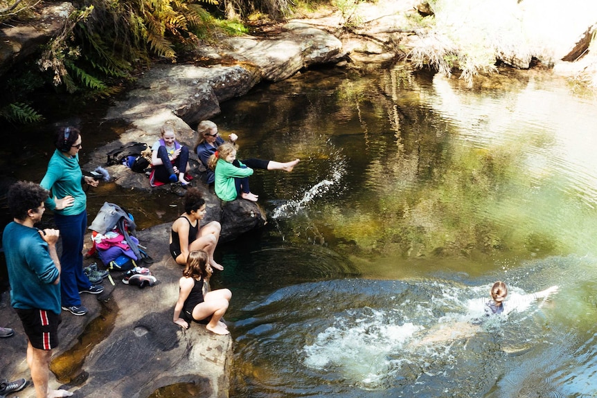 Sarah wears earphones while watching over friends and family jumping into Kingfisher pool.