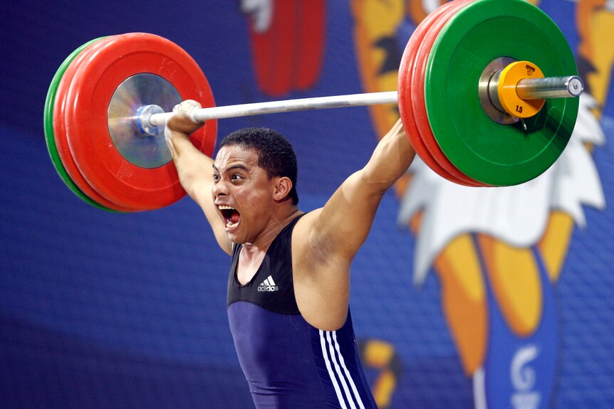A male weightlifter lifts weights above his head and screams in delight.
