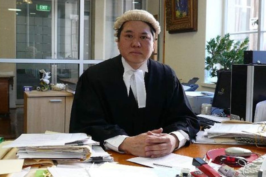 A man wearing a barrister's wig and robes sitting at a desk with papers on it