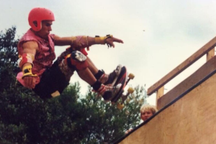 A man wearing a red helmet rides a skate board up a wooden ramp