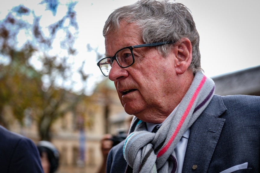An older man with grey hair, glasses and a scarf