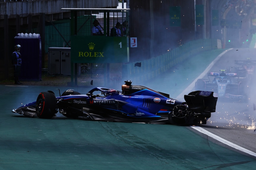 A blue F1 car, spinning on track, damaged, about to drive into barriers