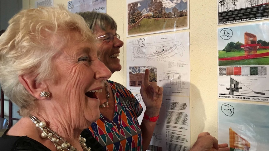 Women looking at a large pinboard covered in designs for public toilets