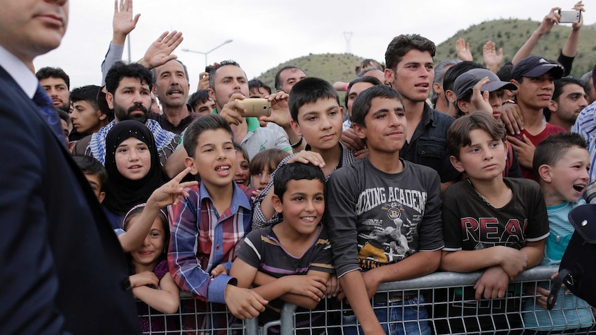 Refugees try to catch a glimpse of the German Chancellor visiting the refugee camp.