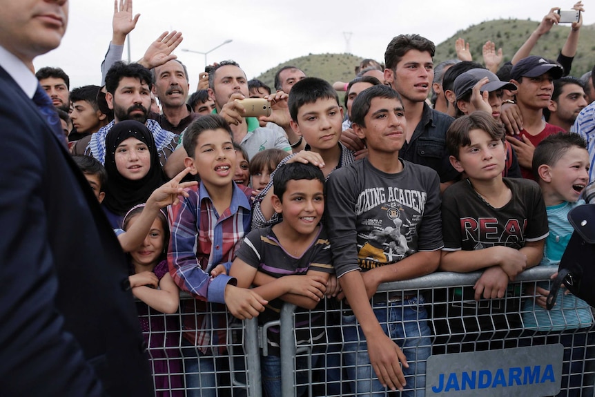 Refugees try to catch a glimpse of the German Chancellor visiting the refugee camp.