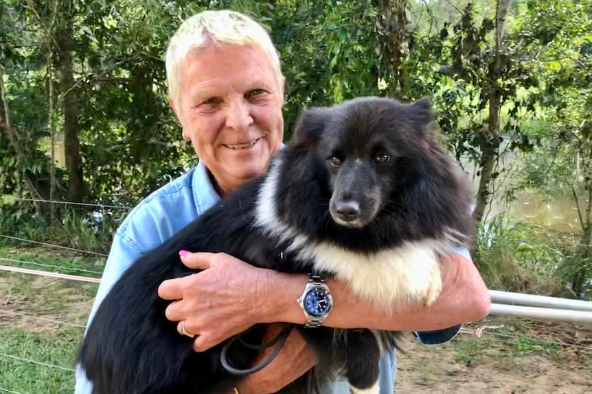 A woman with short hair holds a little black and white dog.