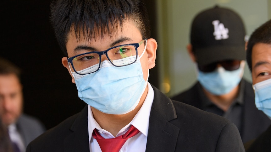 A young man wearing a suit, glasses and face mask