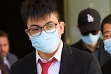 A young man wearing a suit, glasses and face mask