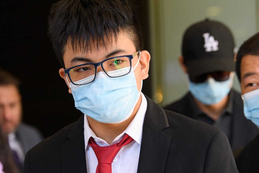 A young man wearing a suit, glasses and face mask