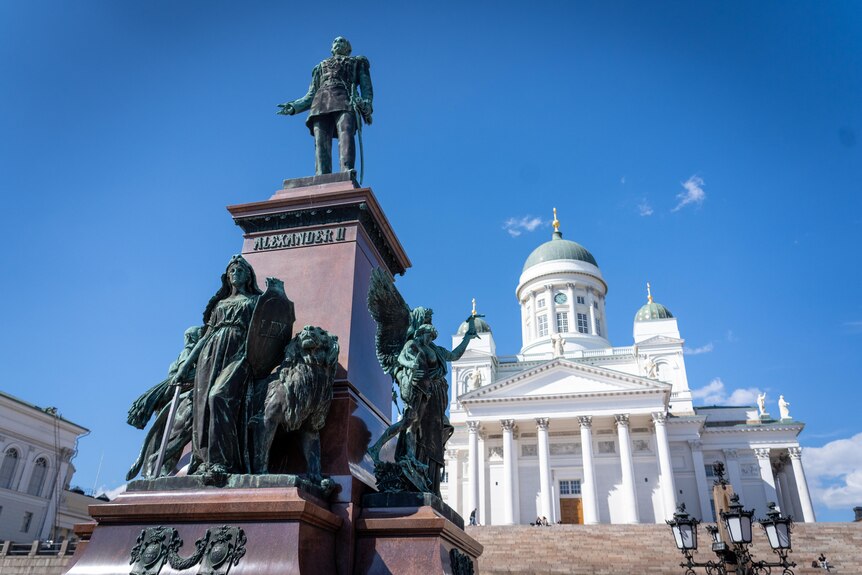 A statue of Alexander II stands in front of a historical white building in Helsinki.