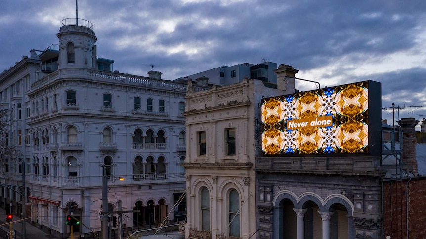 A billboard with the words "Never Alone" on the top of an old building on a cloudy dark day