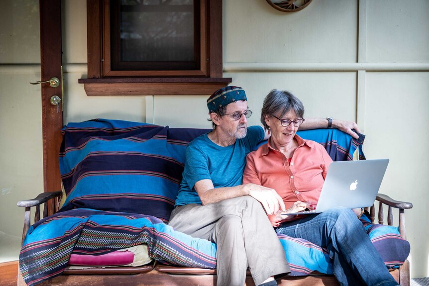 A woman and a man sitting on a couch looking at a laptop.
