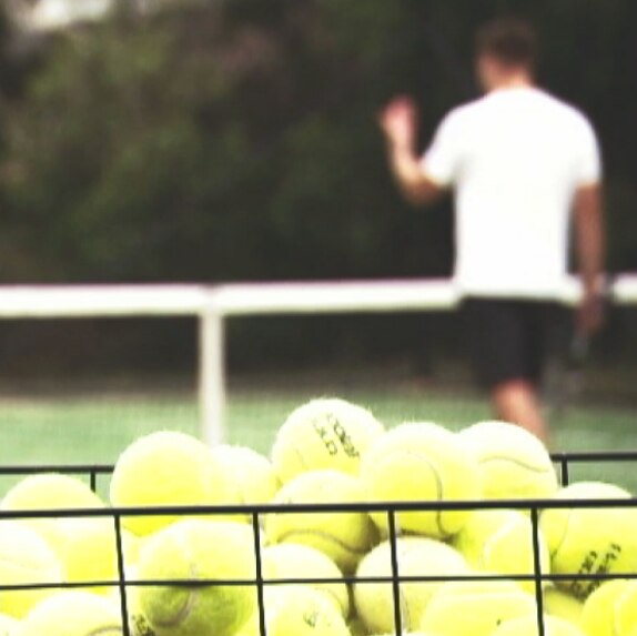 A photo of a basket of tennis balls, with a coach and student out of focus in the background.