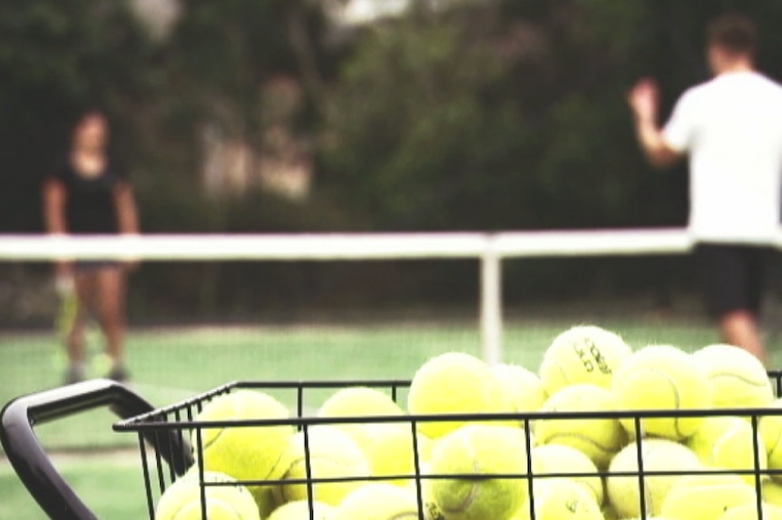 A photo of a basket of tennis balls, with a coach and student out of focus in the background.