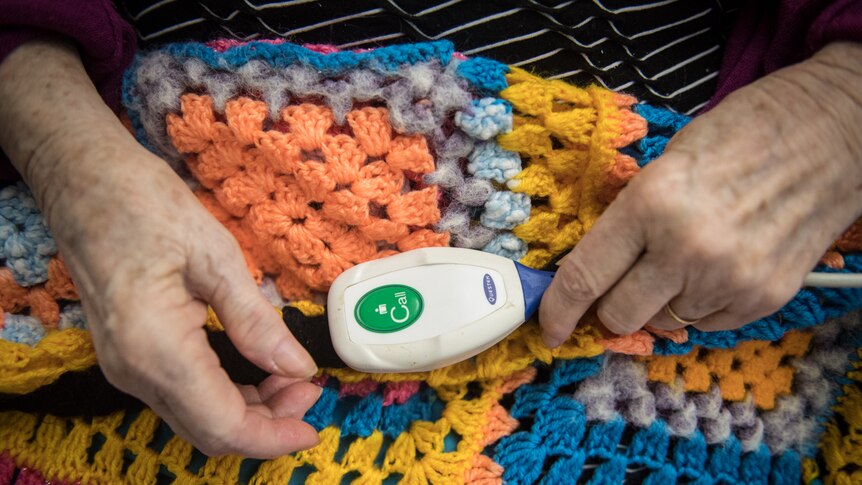A close up of a call button sitting on a knitted blanket in elderly woman's hands.