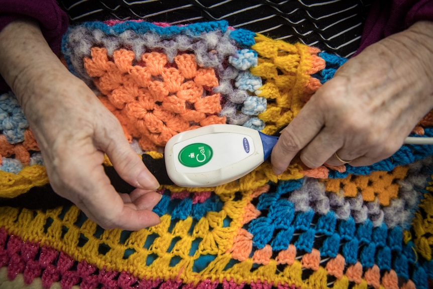 A close up of a call button sitting on a knitted blanket in Dorothy's hands.