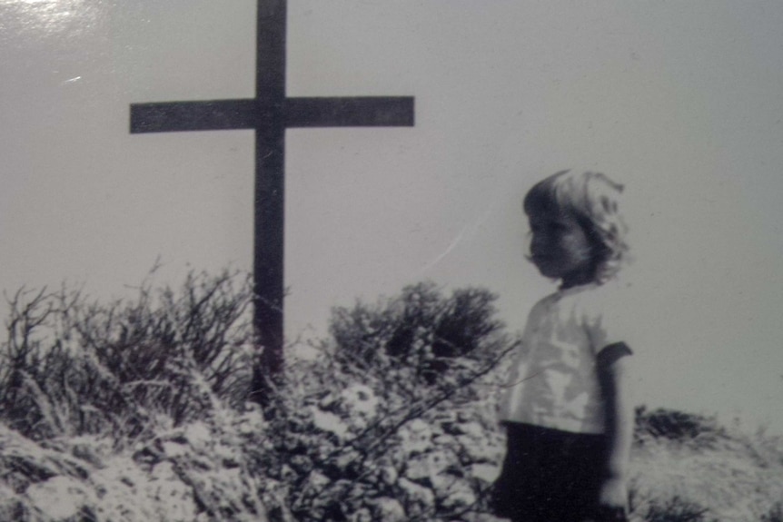 An old photograph of a little boy standing next to a grave