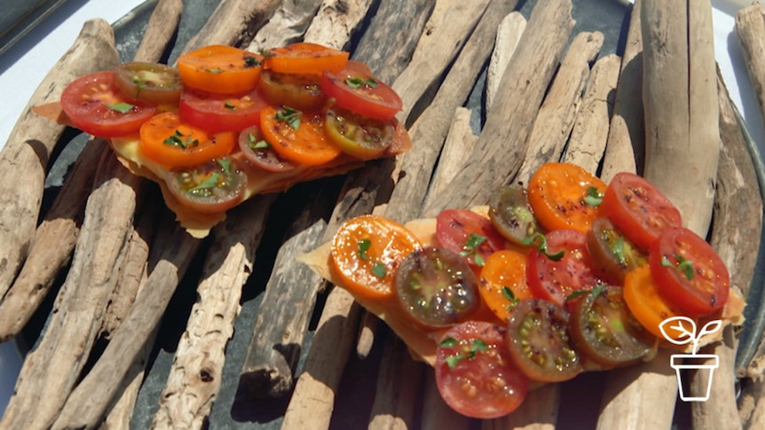 Sliced tomatoes with herbs on top of pastry base presented on a platter made of sticks