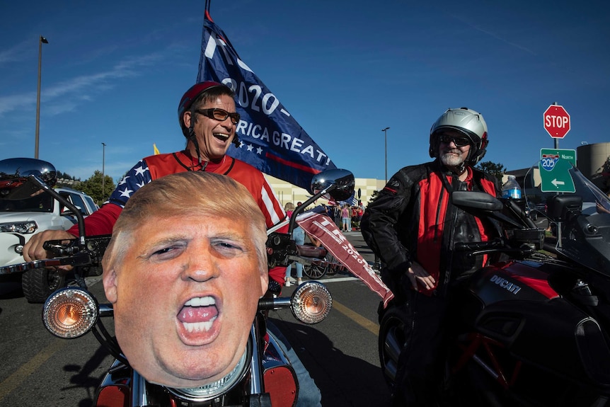 A rider with a huge image of Donald Trump's head rigged to his motorbike smiles.