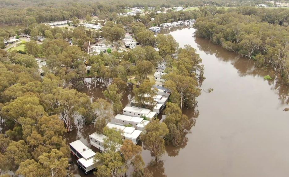 An aerial shot of houses on the edge of a swollen river.
