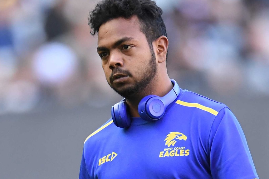 A mid shot of Willie Rioli of the West Coast Eagles wearing a warm-up shirt and headphones on the MCG.