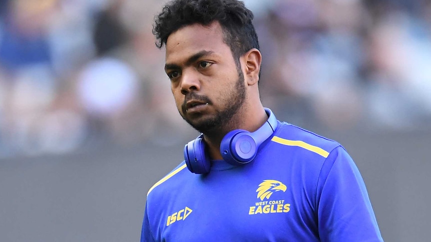 A mid shot of Willie Rioli of the West Coast Eagles wearing a warm-up shirt and headphones on the MCG.