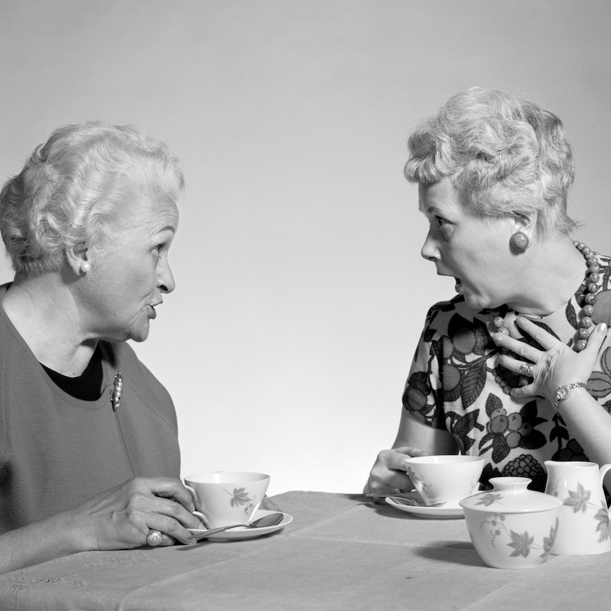 Two older women drinking tea and gossiping, one seems shocked at what the other has said