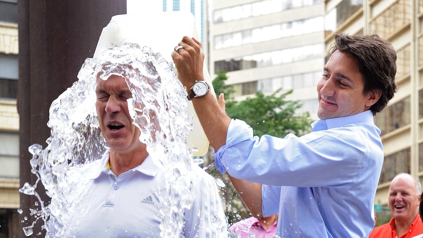 A man dumps a bucket of iced water over the head of another man, who looks shocked.