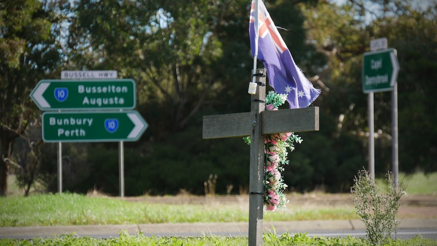 A cross adroned with flowers sits on a grassy road verge