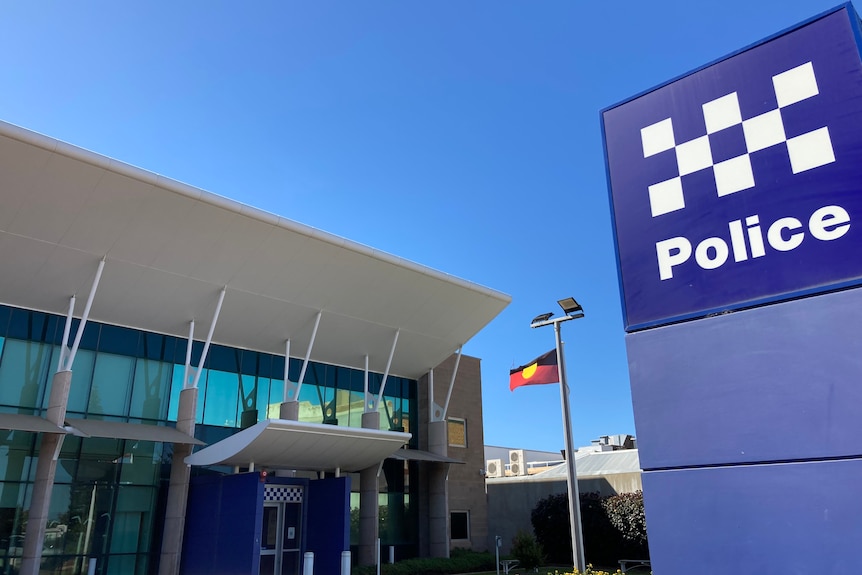 Photo of large police sign in the foreground with the Geraldton police station and indigenous flag in the background.