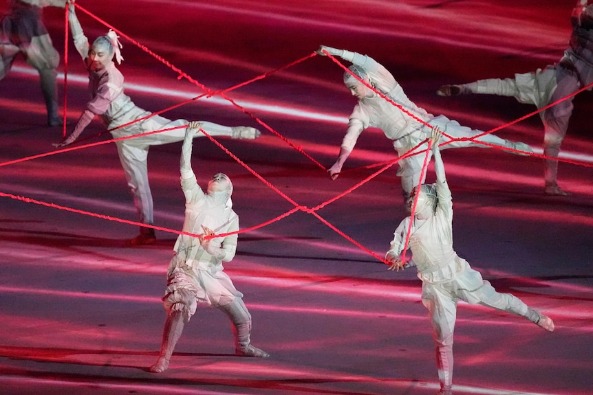 Dancers perform with lengths of red string.